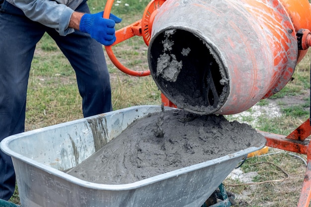 Ein Arbeiter gießt Zementmörtelbeton aus einem Betonmischer in eine Schubkarre Vorbereitung von Zementmörtel auf der Baustelle