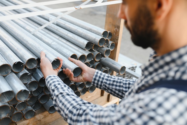 Ein Arbeiter hält Metallrohre in einem Fabriklager Metallwalzen