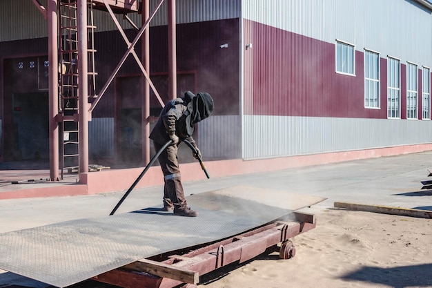 Ein Arbeiter im Spezialanzug sandstrahlt auf einem Industriegelände Metall