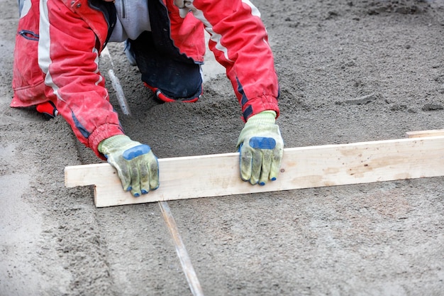 Foto ein arbeiter in einem roten overall kniet und ebnet das sandige fundament mit einem niveau unter den pflasterplatten