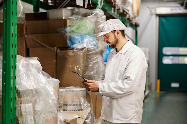 Ein Arbeiter in einer Lebensmittelfabrik überprüft den Lagerbestand, während er ein Tablet in der Hand hält