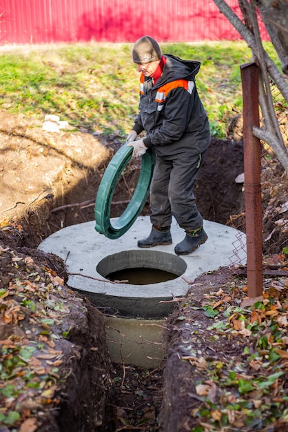 Ein Arbeiter installiert einen Kanalschacht an einer Klärgrube aus Betonringen. Bau von Abwasserentsorgungssystemen für Privathäuser.