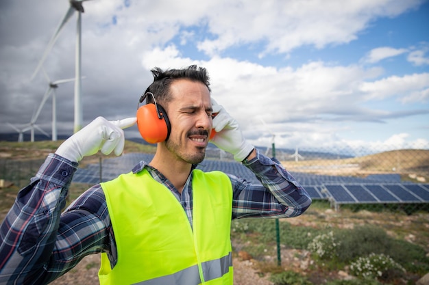 Ein Arbeiter leidet unter Ohrenschmerzen in der Nähe von Windkraftanlagen und trägt daher geräuschunterdrückende Kopfhörer