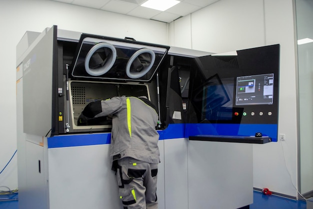 Ein Arbeiter schaut in das offene Fenster des großen Industriedruckers für Metallpulver das Arbeitspr