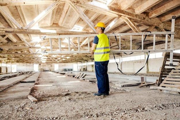 Ein Arbeiter steht mit Leitern in den Händen auf der Baustelle und bereitet sich auf die Arbeit vor