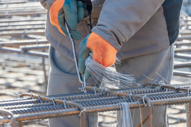 Ein Arbeiter verwendet Stahlbindedraht, um Stahlstäbe an Bewehrungsstäben zu befestigen Nahaufnahme Stahlbetonkonstruktionen Stricken eines Metallbewehrungskäfigs