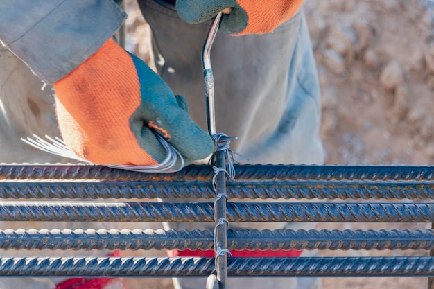 Ein Arbeiter verwendet Stahlbindedraht, um Stahlstäbe an Bewehrungsstäben zu befestigen Nahaufnahme Stahlbetonkonstruktionen Stricken eines Metallbewehrungskäfigs