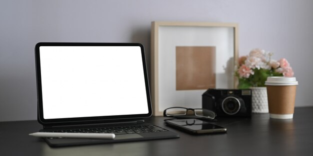 Ein Arbeitsbereich ist von einem weißen Computer-Tablet mit leerem Bildschirm und persönlicher Ausrüstung umgeben.