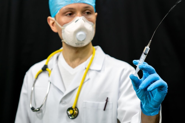 Ein Arzt in einem weißen Kittel und einer Spritze in der Hand Ein Mann in einer medizinischen Maske und einem medizinischen Kittel auf schwarzem Hintergrund Impfung gegen Coronavirus und Covid19