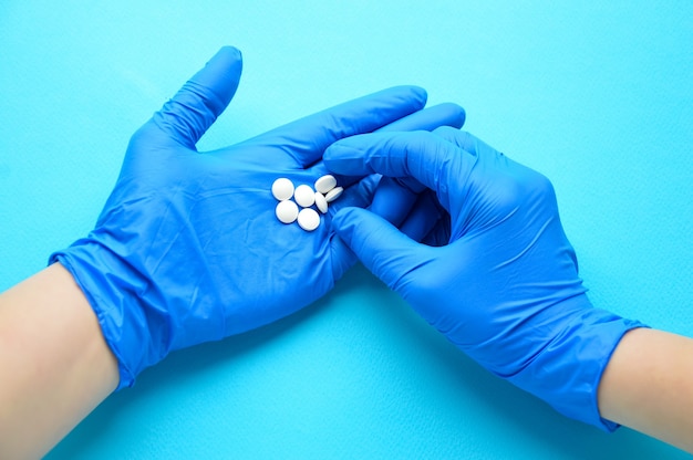 Ein Arzt in medizinischen Handschuhen hält weiße Pillen Blauer Hintergrund
