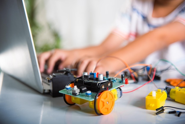 Foto ein asiatischer junge lernt mit einem laptop für ein arduino-roboter auto programmieren und programmieren. kleine kinder tippen mit einem spielzeug auto code in den computer. steam-bildung ki-technologie-kurs schulunterricht