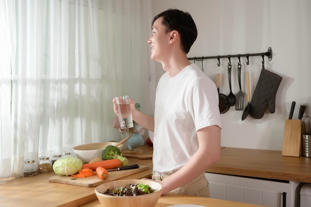 Ein asiatischer junger Mann trinkt frisches Wasser in der Küche zu Hause gesundes Lebensstilkonzept