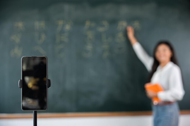 Ein asiatischer Lehrer unterrichtet an Bord, während er im Klassenzimmer über ein Smartphone eine Vorlesung an der Tafel online hält