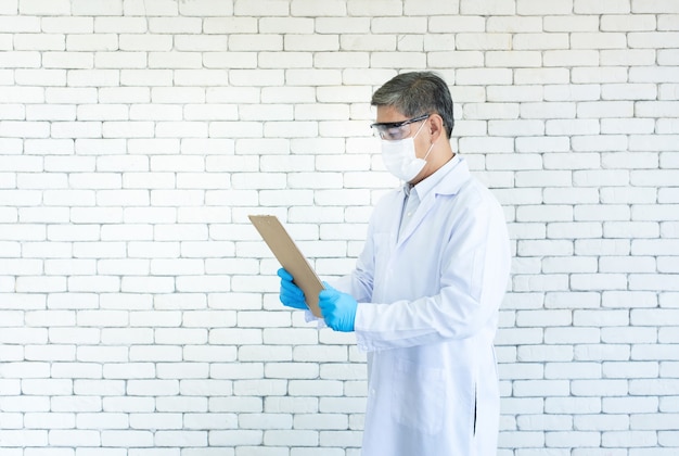 Ein asiatischer männlicher Arzt trägt eine klare Brille und eine Gesichtsmaskenhand, die eine medizinische Karte in einem Krankenhaus hält.