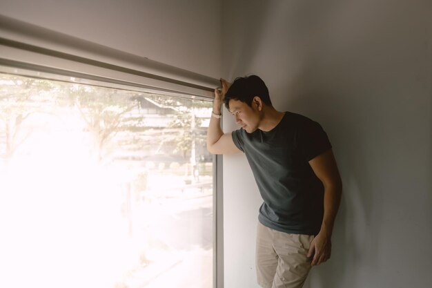 Ein asiatischer Mann, der sich an eine Wand lehnt, starrt aus dem Fenster