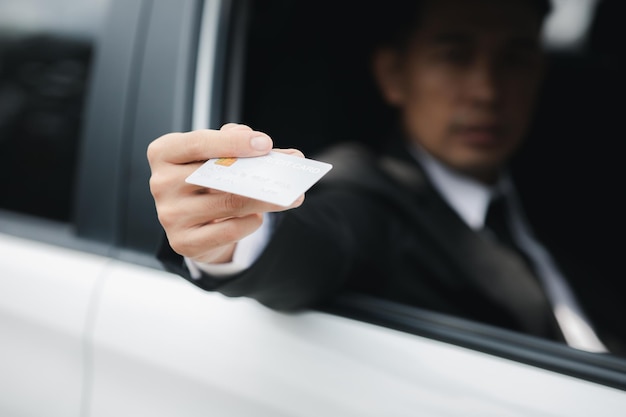 Ein asiatischer Mann in einem formellen Anzug bleibt im Auto und öffnet das Fenster, das ihm seine Kreditkarte überreicht hat, um die Benzinfahrt mit dem Auto zu bezahlen, sicheres Fahren unter Beachtung der Verkehrsregeln