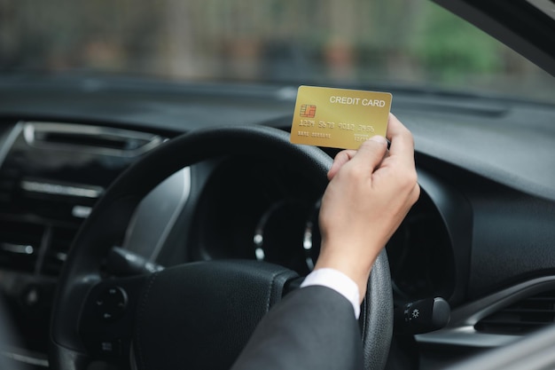 Ein asiatischer Mann in einem formellen Anzug ist in einem Auto, er hält eine Kreditkarte, er fährt in eine Tankstelle und bezahlt seine Kreditkartenrechnungen. Reisen Sie mit dem Auto, sicheres Fahren unter Beachtung der Verkehrsregeln