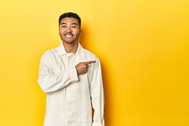 Foto ein asiatischer mann in einem scharfen weißen hemd in einem gelben studio lächelt und weist zur seite, um etwas zu zeigen.