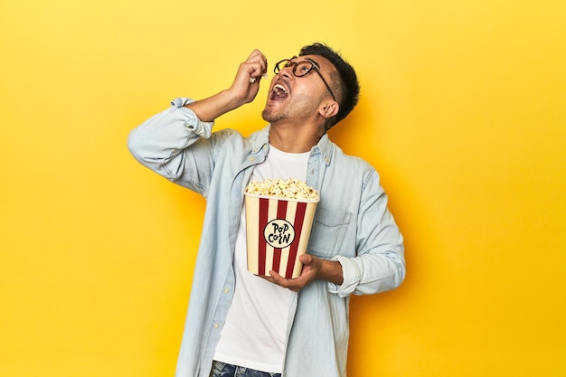 Ein asiatischer Mann isst Popcorn und umarmt ein Kino-Konzept auf einem gelben Studio-Hintergrund