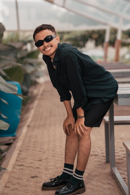 Ein asiatischer Mann mit einem Schnurrbartgesicht, der ein Hemd und eine Sonnenbrille trägt, während er mit seinen Freunden in einem Café rumhängt