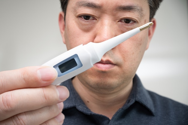 Ein asiatischer Mann mittleren Alters, der besorgt auf das Thermometer in seiner Hand schaut