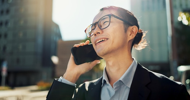 Ein asiatischer Mann telefoniert und lacht in der Stadt, um einen lustigen Witz zu unterhalten oder sich im Freien zu vernetzen. Ein glücklicher Geschäftsmann lächelt und spricht mit seinem Smartphone, um eine lustige geschäftliche Diskussion in einer städtischen Stadt zu führen.