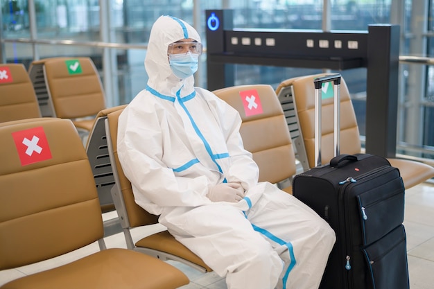 Ein asiatischer Mann trägt einen Ppe-Anzug auf dem internationalen Flughafen, Sicherheitsreisen, Covid-19-Schutz und soziales Distanzierungskonzept