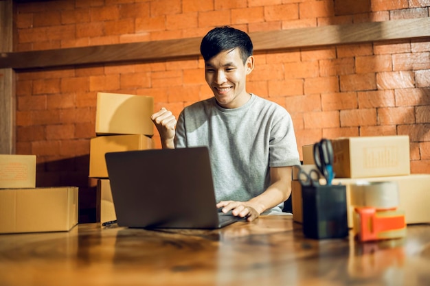 Ein asiatischer Mann verwendet ein Mobiltelefon, um Bestellungen entgegenzunehmen und Artikel in einer Box anzuzeigen, die Live-Streaming-Videos online im asiatischen Online-Markt-Lieferkonzept des Ladenbesitzers aufzeichnet