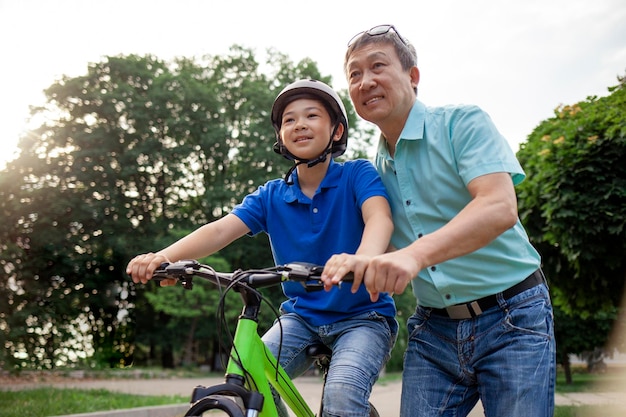 Ein asiatischer Vater lehrt seinen Sohn, Fahrrad zu fahren. Ein koreanischer Senior hilft einem Kind, einem Jungen mit Helm.