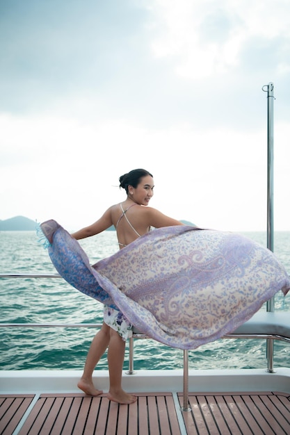 Ein asiatisches Mädchen auf einem Yachtstand, um die frische Luft aus dem Meer mit einem Schal zu empfangen, der flog