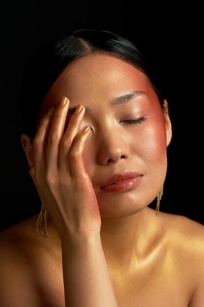 Foto ein asiatisches mädchen auf schwarzem hintergrund im studio gold dünne schlüsselbeine das reich der schönheit und des parfüms berührt sanft ihr gesicht