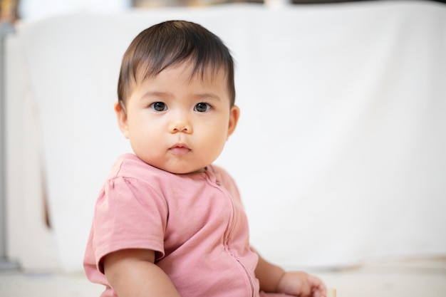 Ein asiatisches Mädchen, etwa 1 Jahr alt, spielt im Wohnzimmer des Hauses. Ein süßes Baby, das ein rosa Kleid trägt. Bleibe bei den Eltern im Haus