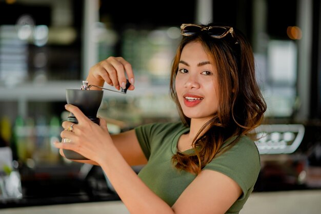 Ein asiatisches Mädchen mahlt schwarzen Kaffee mit einem Handkaffeemühler am Morgen des Hauptstadttages