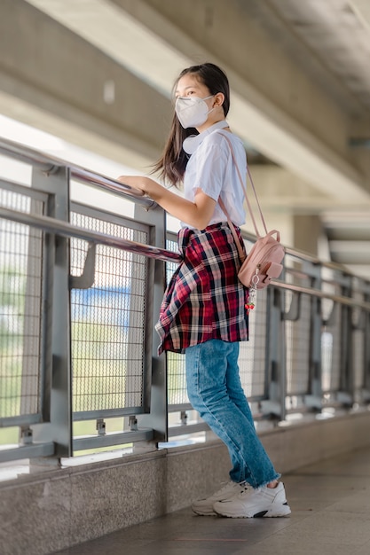 Ein asiatisches Mädchen mit Maske läuft niedergeschlagen auf einem Steg.