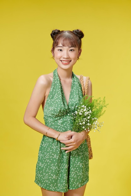 Ein asiatisches Mädchen steht auf gelbem Hintergrund, umarmt einen Blumenstrauß und lächelt in die Kamera