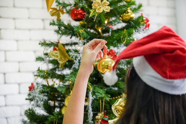 Ein asiatisches Mädchen verziert einen schönen Chrismas-Baum für einen Familienteil.