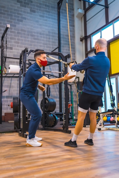 Ein Athlet mit einem Trainer im Fitnessstudio, der Armübungen bei der Coronavirus-Pandemie macht