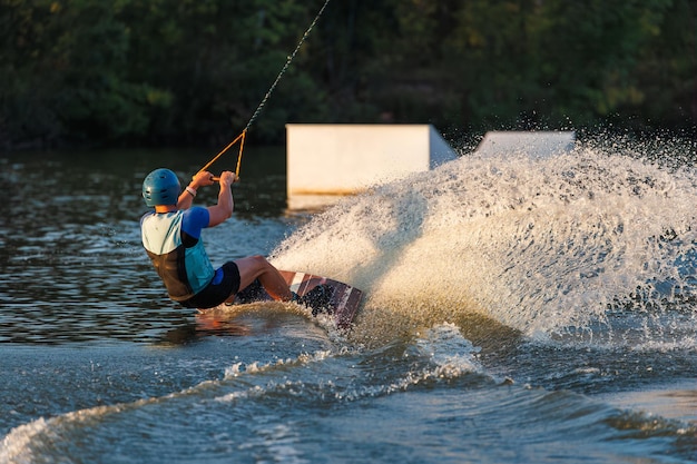 Ein Athlet springt bei Sonnenuntergang über das Wasser im Wakeboard-Park. Der Fahrer führt einen Trick auf dem Brett aus