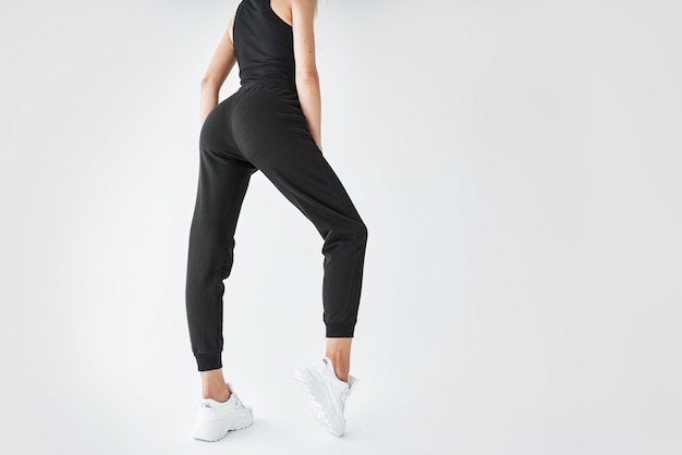 Ein athletisches junges Mädchen trägt dunkelschwarze Hosen, Textilhose für Yoga, Laufen und Sport. Eine fitte junge Frau steht in modernen Joggern. Horizontales Studiofoto des Kleidungsmodells.