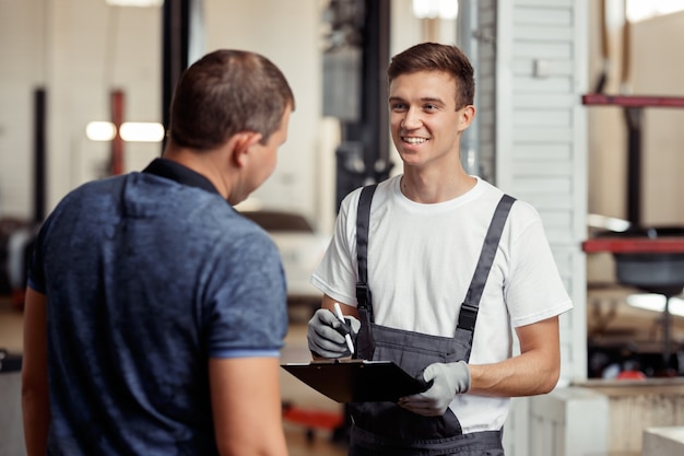 Ein attraktiver Automechaniker lächelt seinen Kunden während des Termins an.