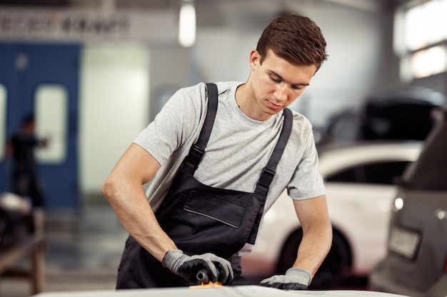 Ein attraktiver Automechaniker poliert bei seiner Arbeit ein Auto. Autoservice und Wartung.