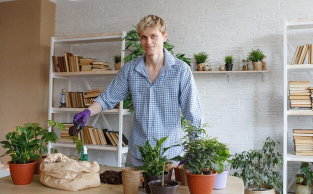 Ein attraktiver junger Mann, der sich um heimische Pflanzen kümmert, verpflanzt Blumen und gießt Erde in Blumentöpfe