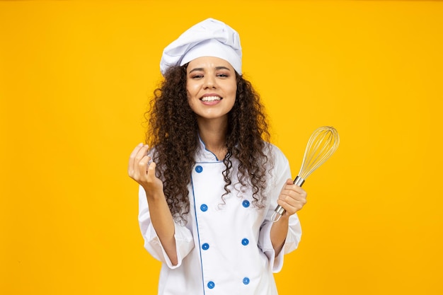 Ein attraktives junges Mädchen in der Uniform eines Kochs mit einem Schneebesen in der Hand