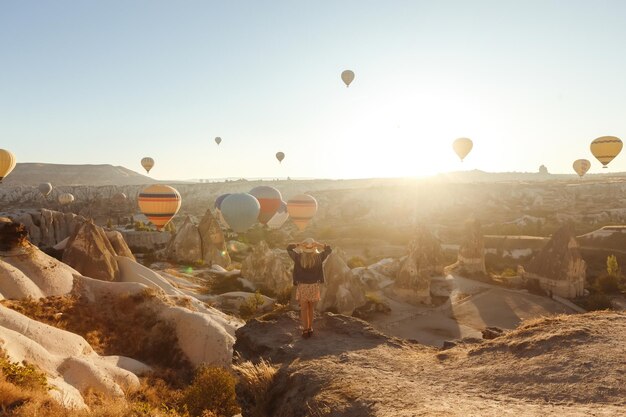 Ein attraktives junges Mädchen steht auf dem Berg mit fliegenden Luftballons, Blick von hinten, Kappadokien