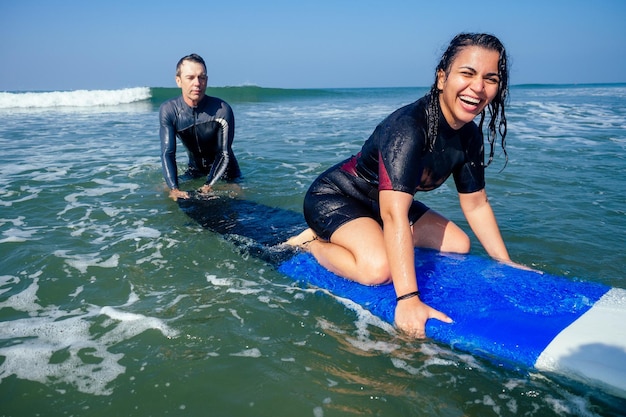 Ein Ausbilder, der einer Inderin im Surfkurs im Meer von Goa demonstriert, wie man auf dem Surfbrett aufsteht