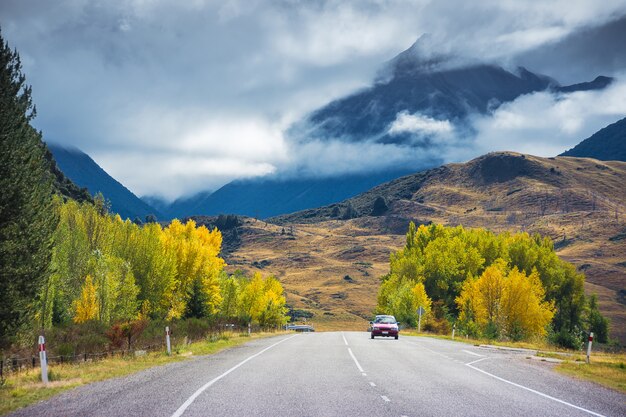 Ein Auto, das auf Straße in Arthurs-Durchlauf, Neuseeland mit bunten Bäumen im Herbst läuft.