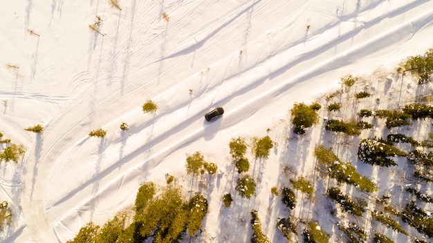 Ein Auto fährt auf einer Landstraße durch den Winterwald, Top-View von einer Drohne