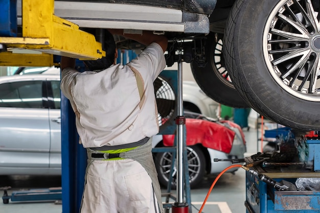 Ein Automechaniker, der unter dem Auto steht, das auf Hebebühne, Autoreparatur ist