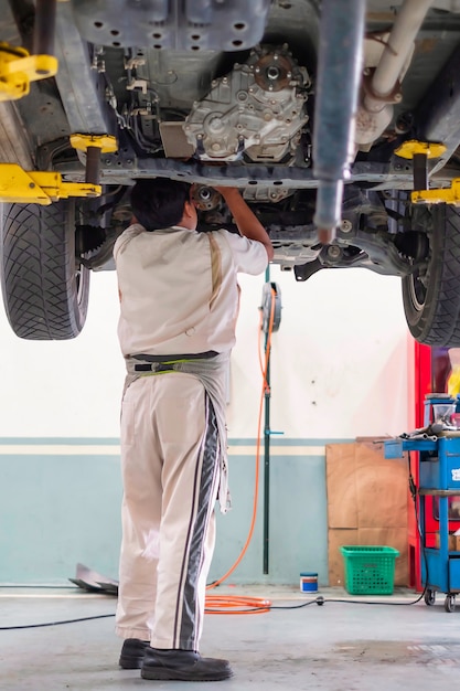 Ein Automechaniker, der unter dem Auto steht, das auf Hebebühne, Autoreparatur ist