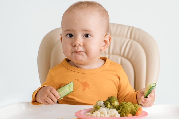 Ein Baby auf einem Fütterungsstuhl isst eine Gurke Das Konzept der richtigen Babynahrung